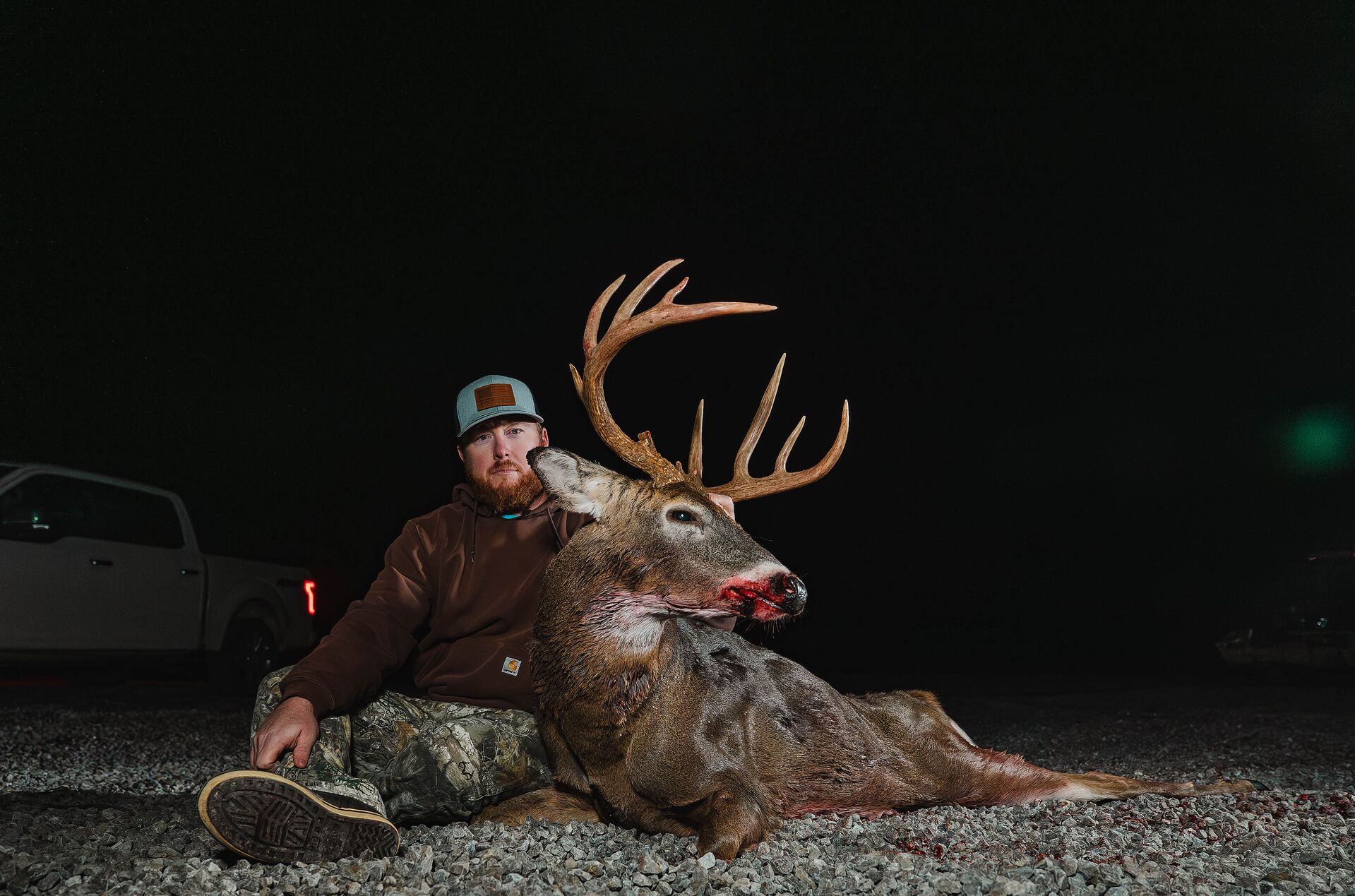 Hunter sits with buck deer after hunt at night, hunting license reciprocity between states concept.