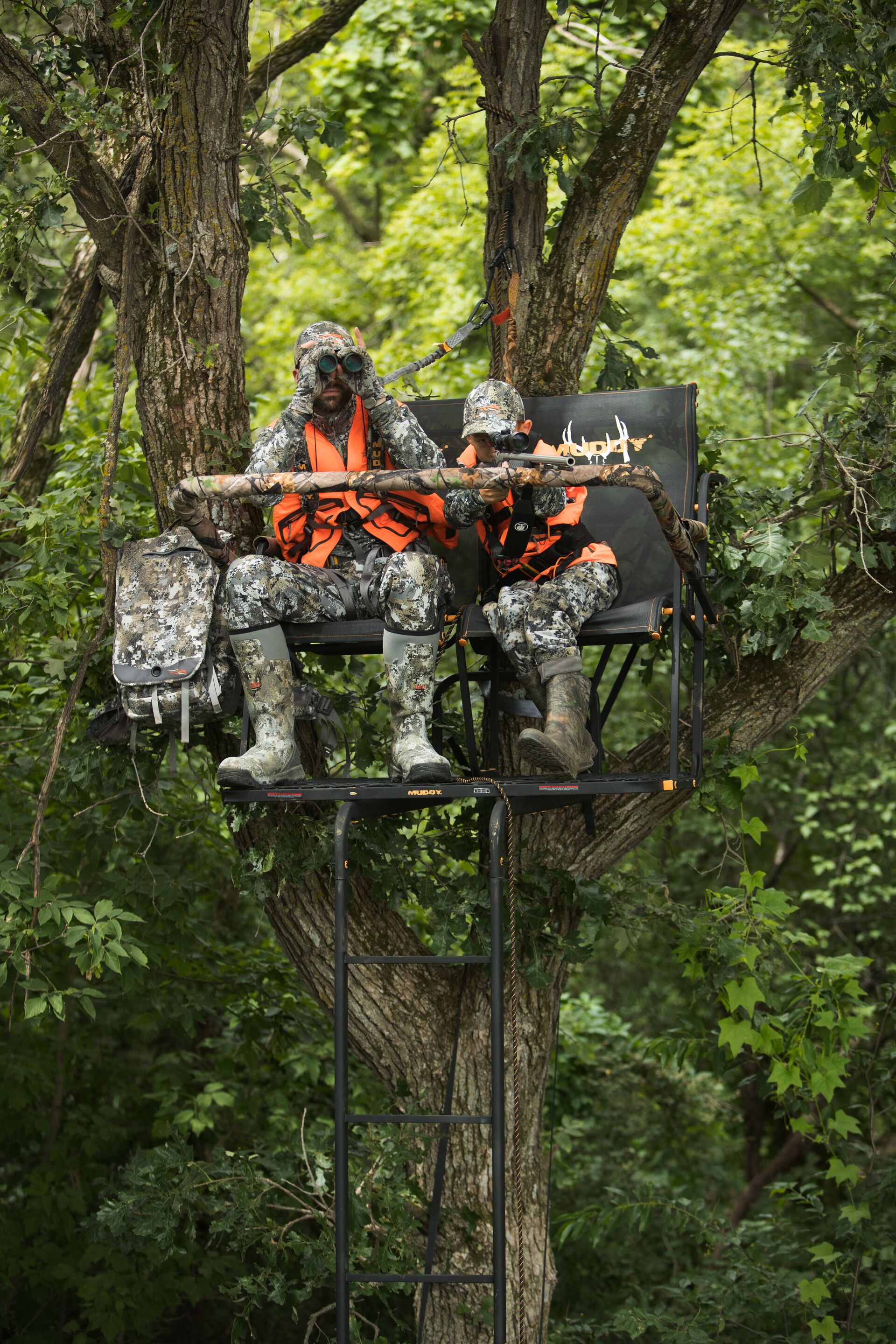 Man and boy with firearms in tree stand, how to haul hunting equipment into tree stand concept. 