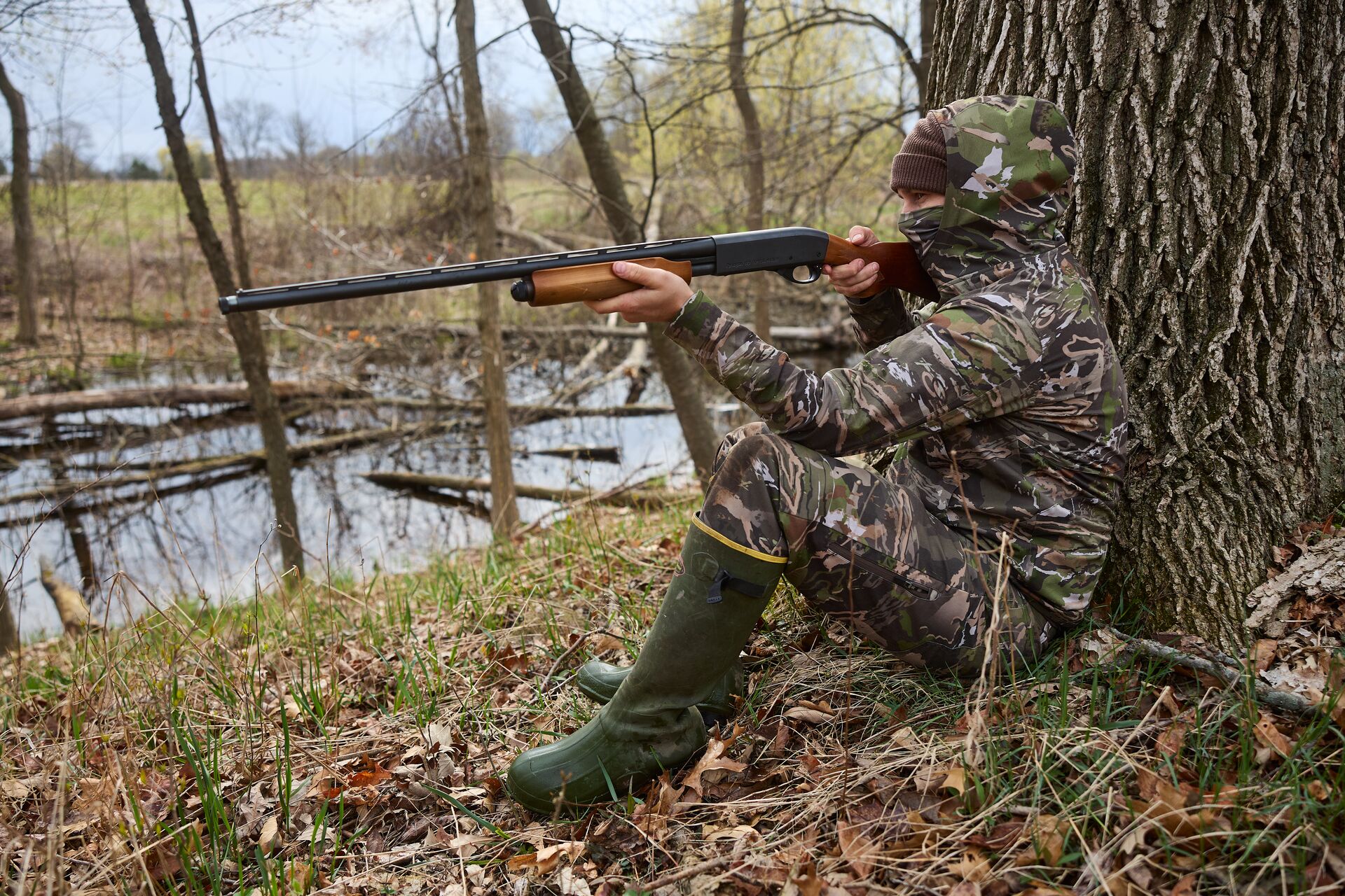 Hunter in camo against tree aims shotgun, Texas hunters safety course online concept.