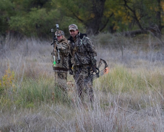 A woman draws a bow while a man watches, hunter safety concept. 